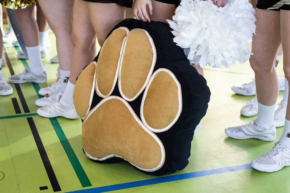 Paw-Print-Kissen auf dem Boden, umgeben von Cheerleader-Beinen in Sportschuhen und einer Pompom.